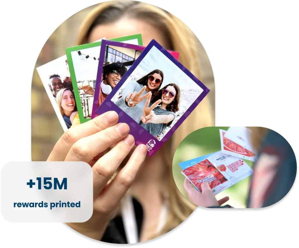 A person holding a fan of colorful printed photo cards, each featuring smiling people in various settings. The largest card in front shows two women making peace signs. In the corner, an inset image shows someone holding printed photo rewards with branded advertisements on the back. A text overlay reads “+15M rewards printed.”